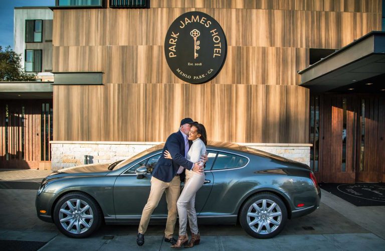 Man embracing a woman in front of their car at the port au cochere of the Park James Hotel.
