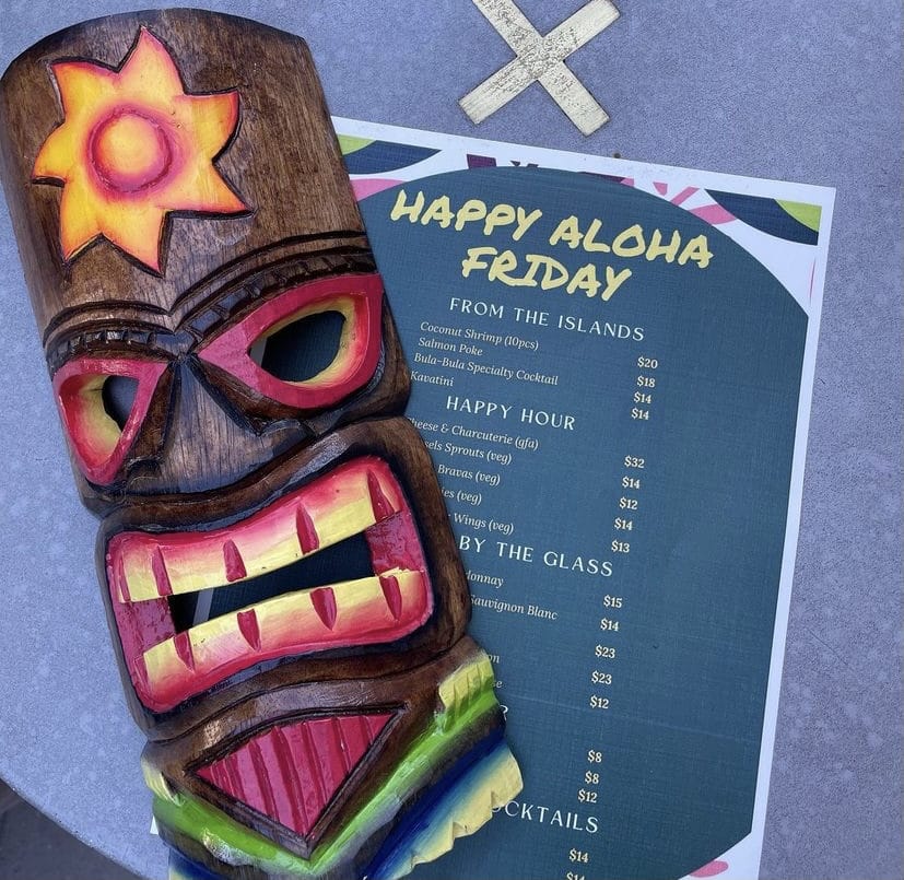 Tiki idol in front of a menu that reads Happy Aloha Friday.