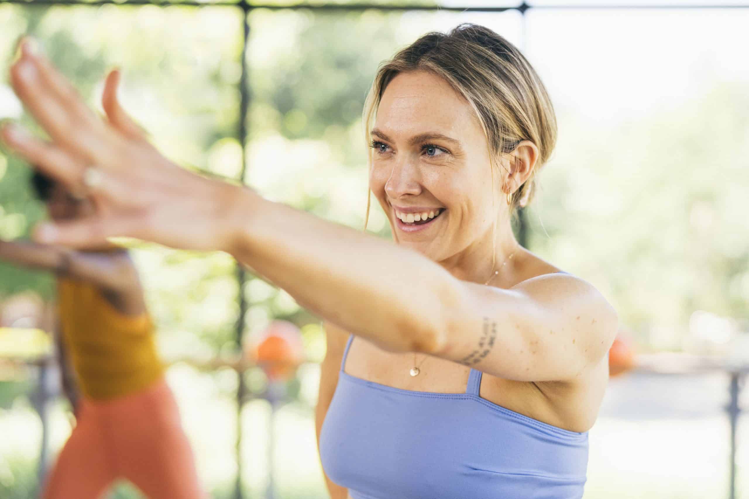 Woman smiling with arm extended doing a Barre class.