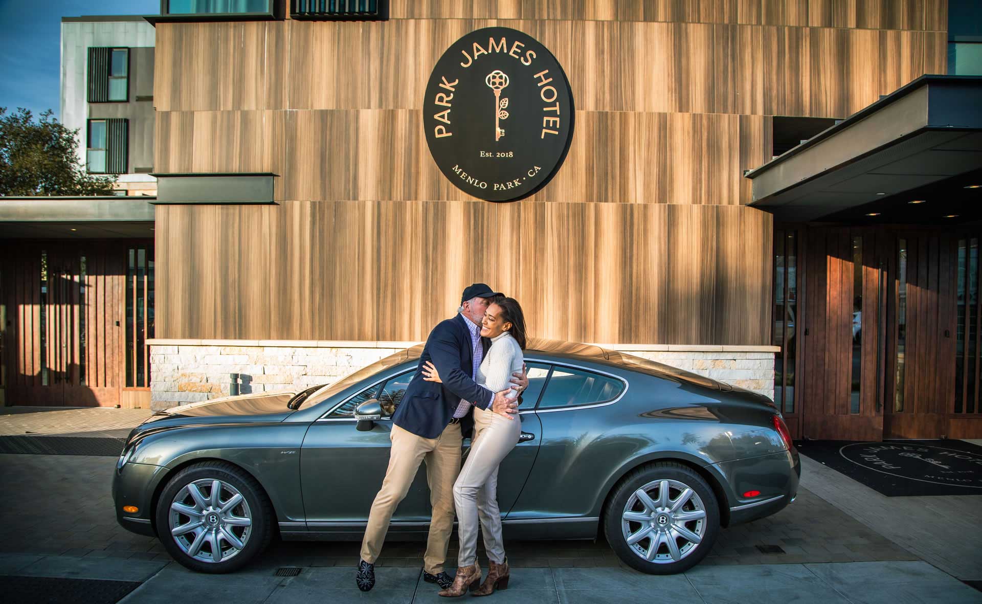 Man embracing a woman in front of their car at the port au cochere of the Park James Hotel.